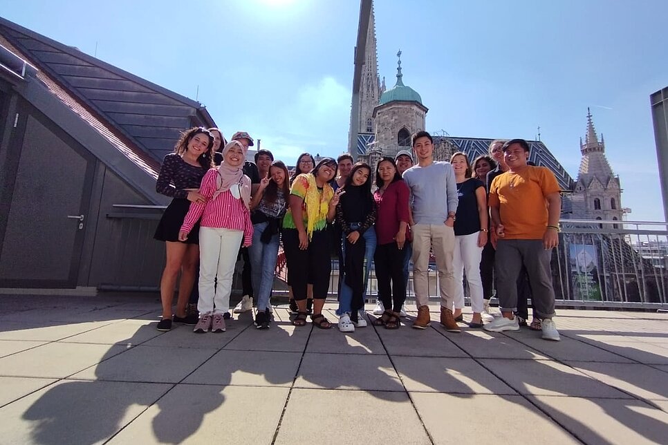 Eine Menschengruppe posiert für ein Foto auf einem Dach mit Blick auf den Stephansdom.