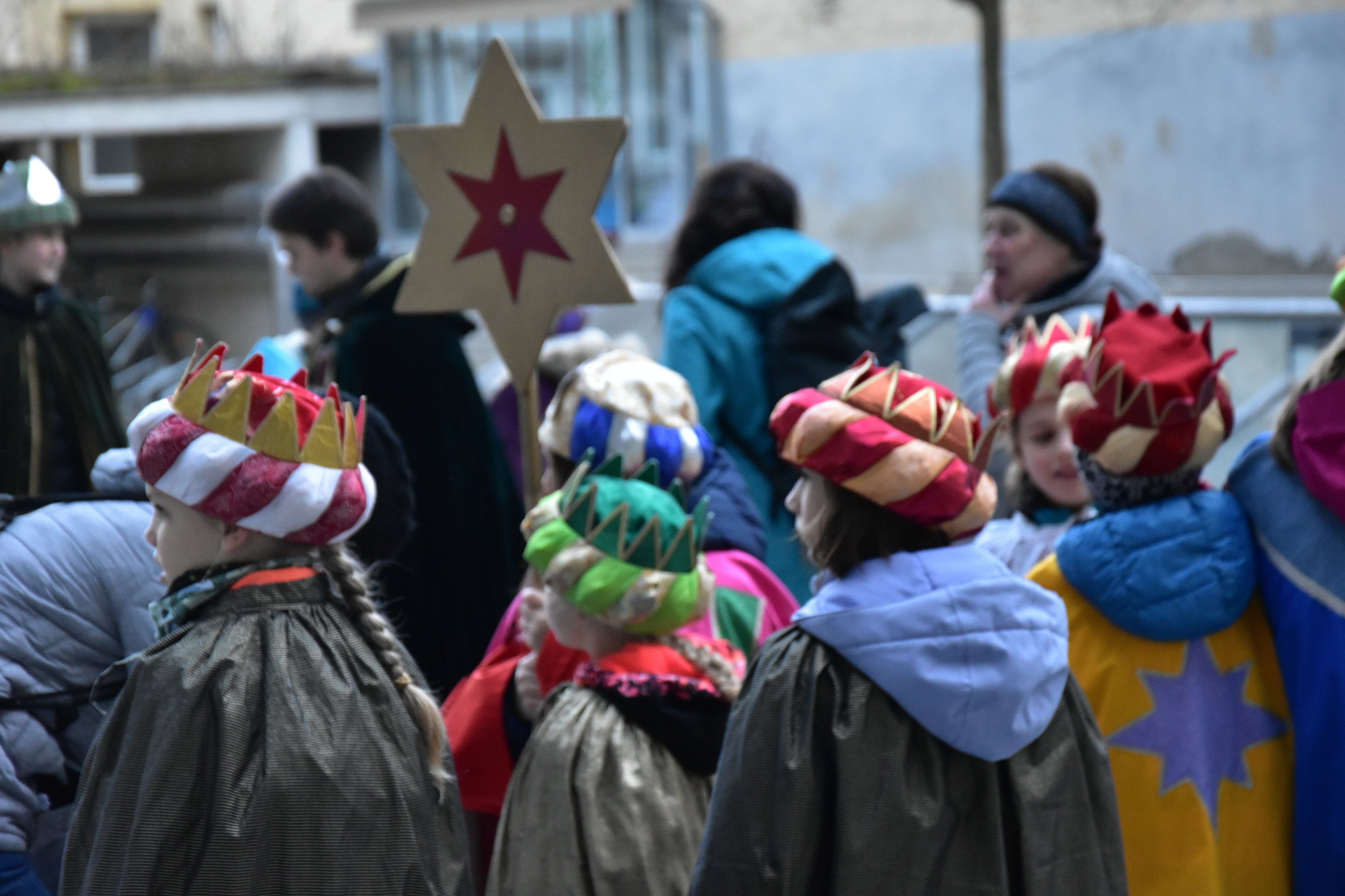 Das Bild zeigt eine Gruppe von Kindern, die als Sternsinger verkleidet sind. Sie tragen bunte Umhänge und Kronen sowie einen Stern, der auf einem Stab gehalten wird.