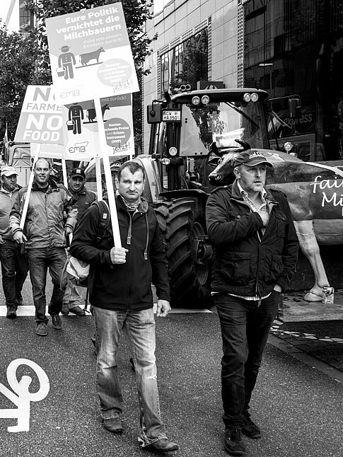 Eine Gruppe von Menschen geht die Straße entlang und hält Schilder in den Händen, die ihre Botschaften präsentieren, wie "Eure Politik vernichtet die Milchbauern." oder "No Farmers, No Food".