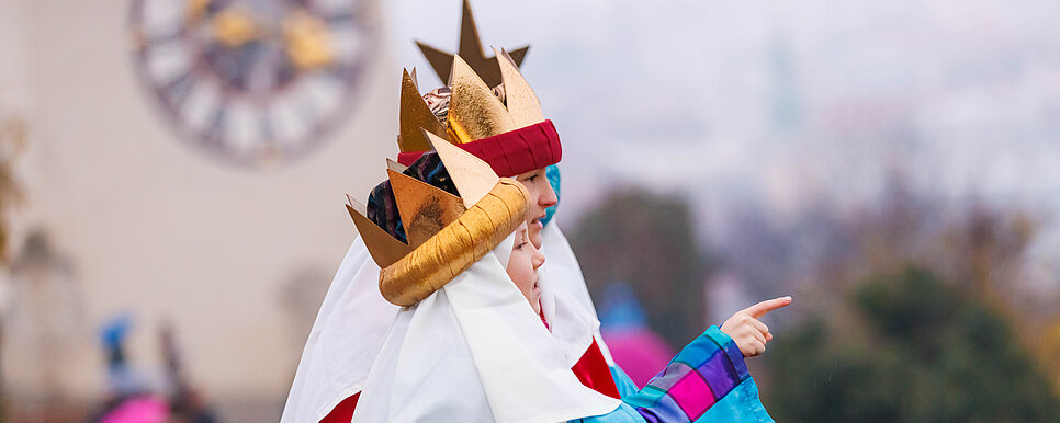 Zwei Kinder mit goldenen Kronen schauen von einer Aussichtsplattform aus auf die Stadt herab.