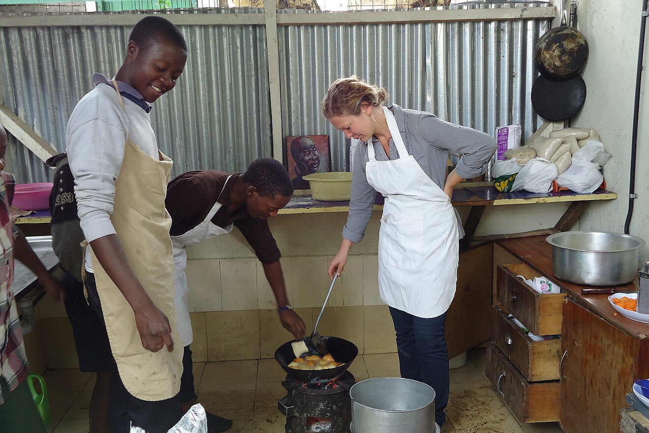 Catering Jugendliche von MSDP kochen gemeinsam mit einer SolidarEinsatz Teilnehmerin auf einem Gaskocher.