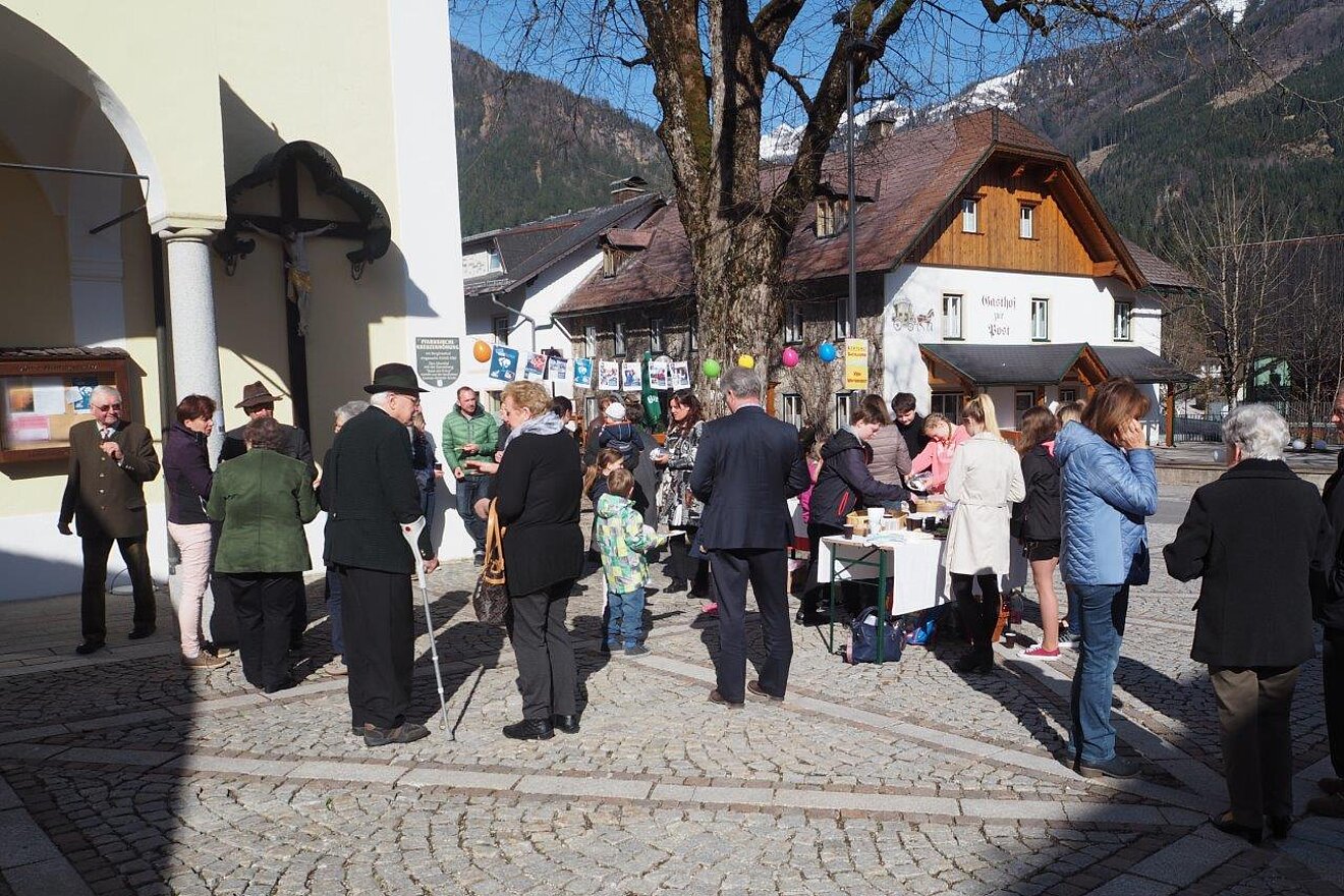 Der Erlös des Buffets nach der Messe in Hinterstoder unsterstützt Mädchen in Nairobi das Leben auf der Straße hinter sich zu lassen. Foto: Wagner Ein Kirchenvorplatz auf dem bei kleinen Ständen viele Menschen stehen.