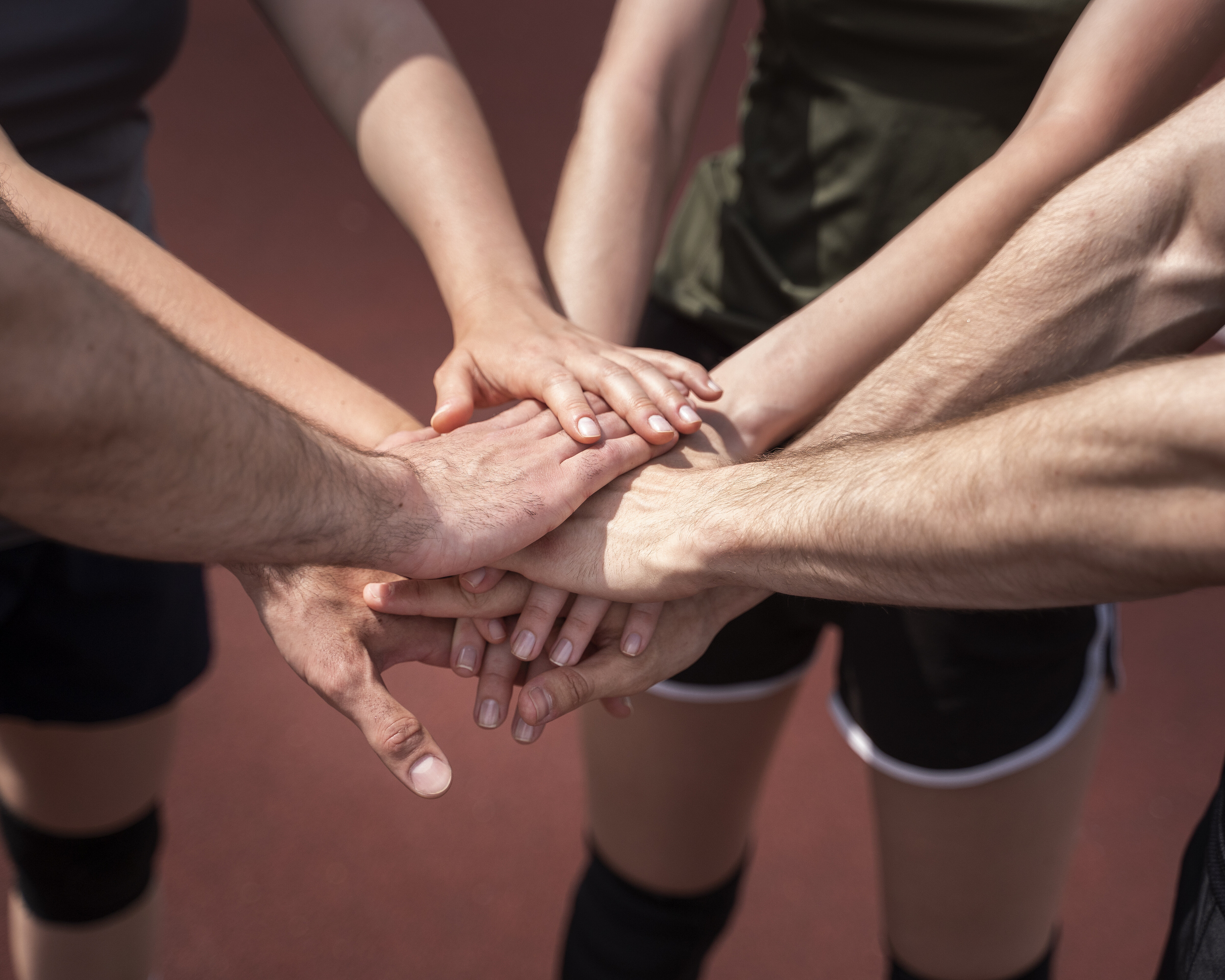 Mehrere Menschen halten ihre Hände auf einem Sportplatz in die Mitte. Es ist ein Zeichen von Gemeinschaft.